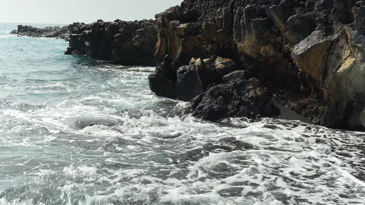 Onda scura si infrange e sbatte contro la roccia vulcanica nera a Tenerife.