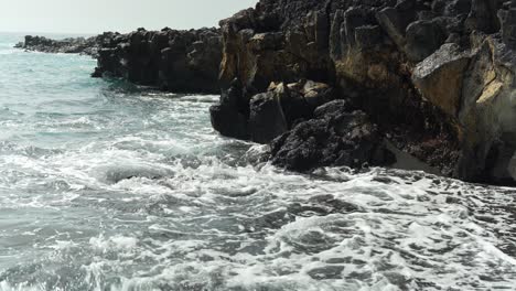 dark wave splashes and crashes against black volcanic rock in tenerife