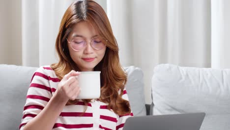 young woman enjoying a cup of tea while using notebook to chat with friends