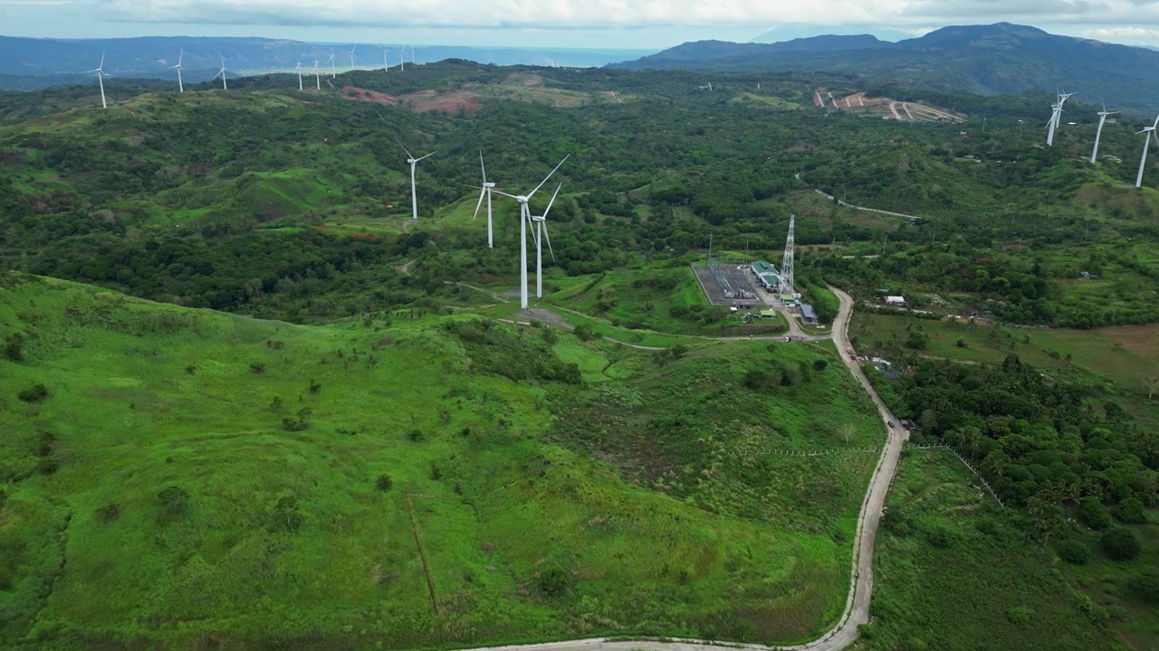 Scenic aerial view of wind turbines on green hills in Pililla, Rizal during daytime with a tropical mountain backdrop.