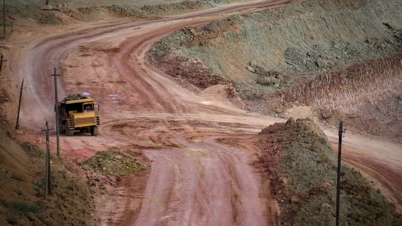 Mid shot of heavy mining trucks carring cargo in opencast mining quarry in sunny summer day. Bouxite mining quarry.
