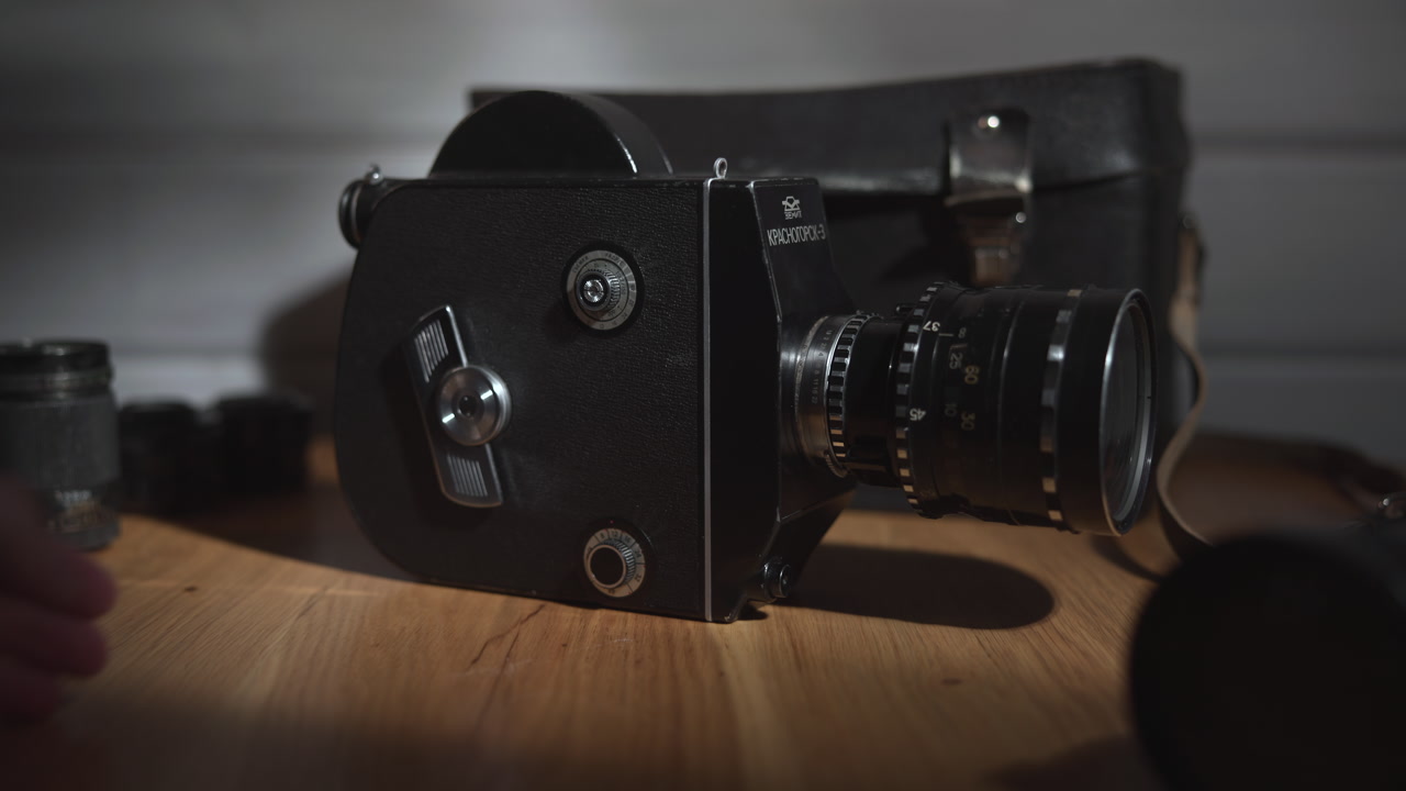 Vintage Film Camera On Wooden Table, Filmmaker Hand Winds Crank And Inspects Lens, Textured Metal Body . Media