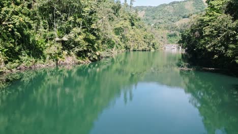 Green-reflective-pond-in-tropical-rainforest-panorama,-aerial-dolly-in