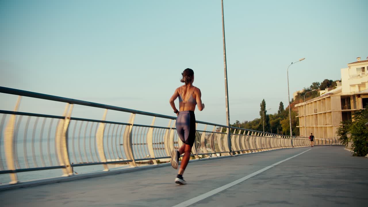 una chica en un uniforme deportivo de verano corre a lo largo del puente. correr por la mañana en la ciudad
