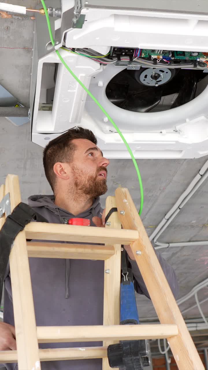 Technician Installing Air Conditioning Unit on Ceiling from Ladder