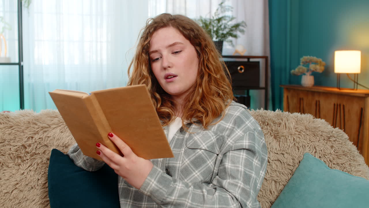 Woman sitting on sofa opening and reading book with focus thoughtfully flipping pages and reflecting