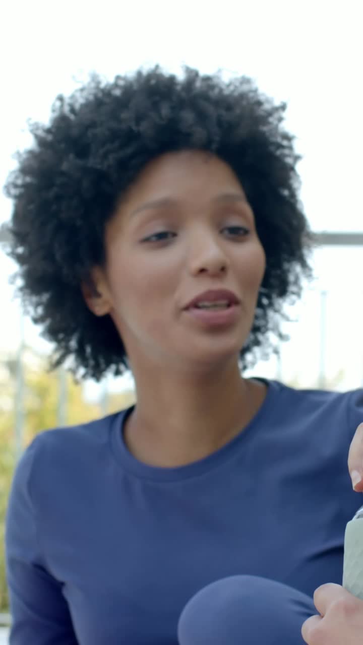 Vídeo vertical: Mulher de azul se esticando perto do corrimão, pegando garrafa de um amigo para beber, usando relógio