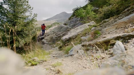 Adult-male-hiker-with-sticks-walking-on-rocky-trail-in-Lagorai-mountain-chain-during-cloudy-day