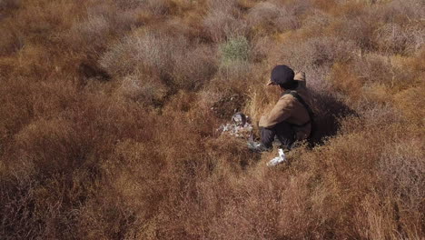 halconero macho joven con sentadillas de halcón de entrenamiento en campo de cepillo marrón seco