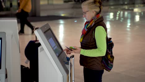 foto alta de una mujer con pasaporte y teléfono inteligente en la mano, en una terminal de auto check in del aeropuerto y registrándose a sí misma
