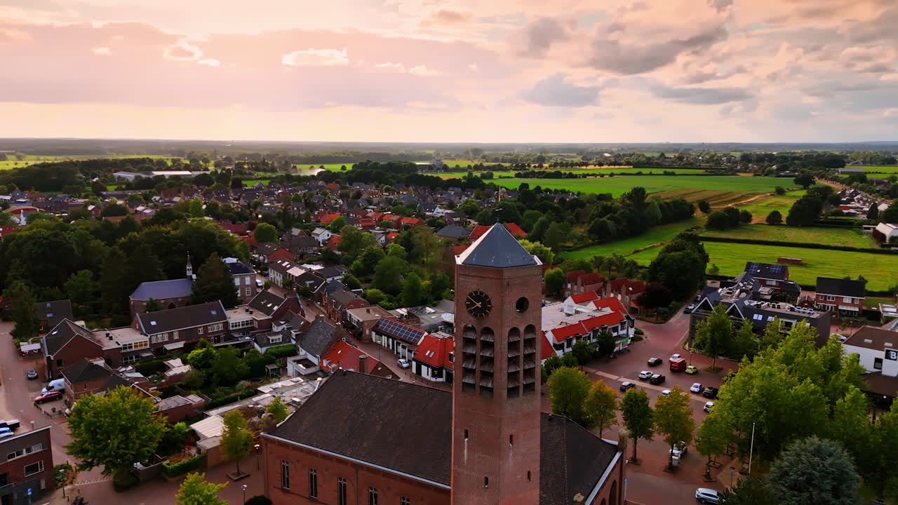 Tower of Saint Lawrence Church with a weathercock on top. Picturesque green town panorama at backdrop. Vierlingsbeek, Netherlands. Aerial view