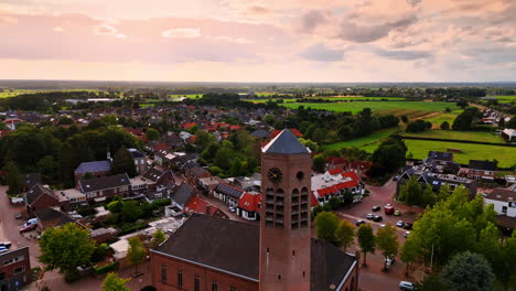 tower of saint lawrence church with a weathercock on top. picturesque green town panorama at backdrop. vierlingsbeek, netherlands. aerial view