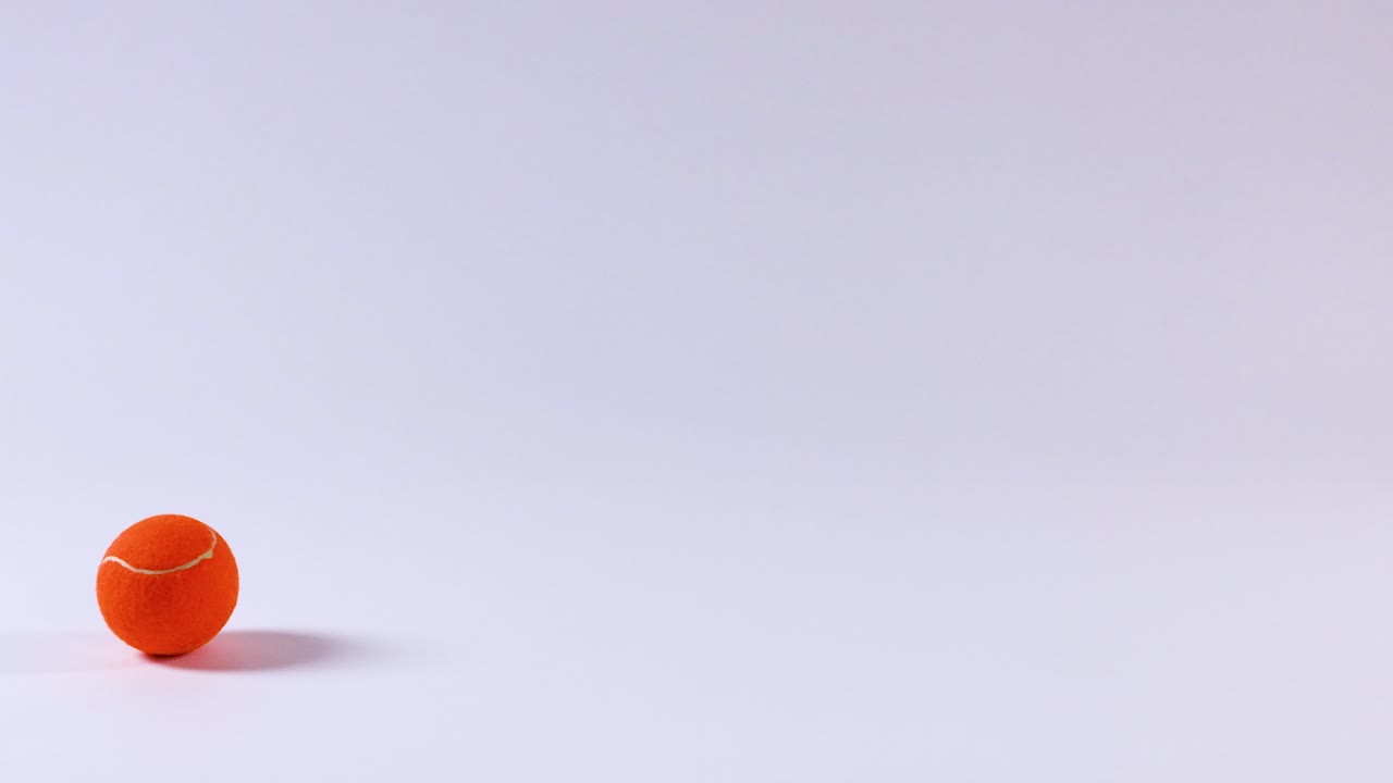 una pelota de tenis naranja rodando sobre una superficie blanca