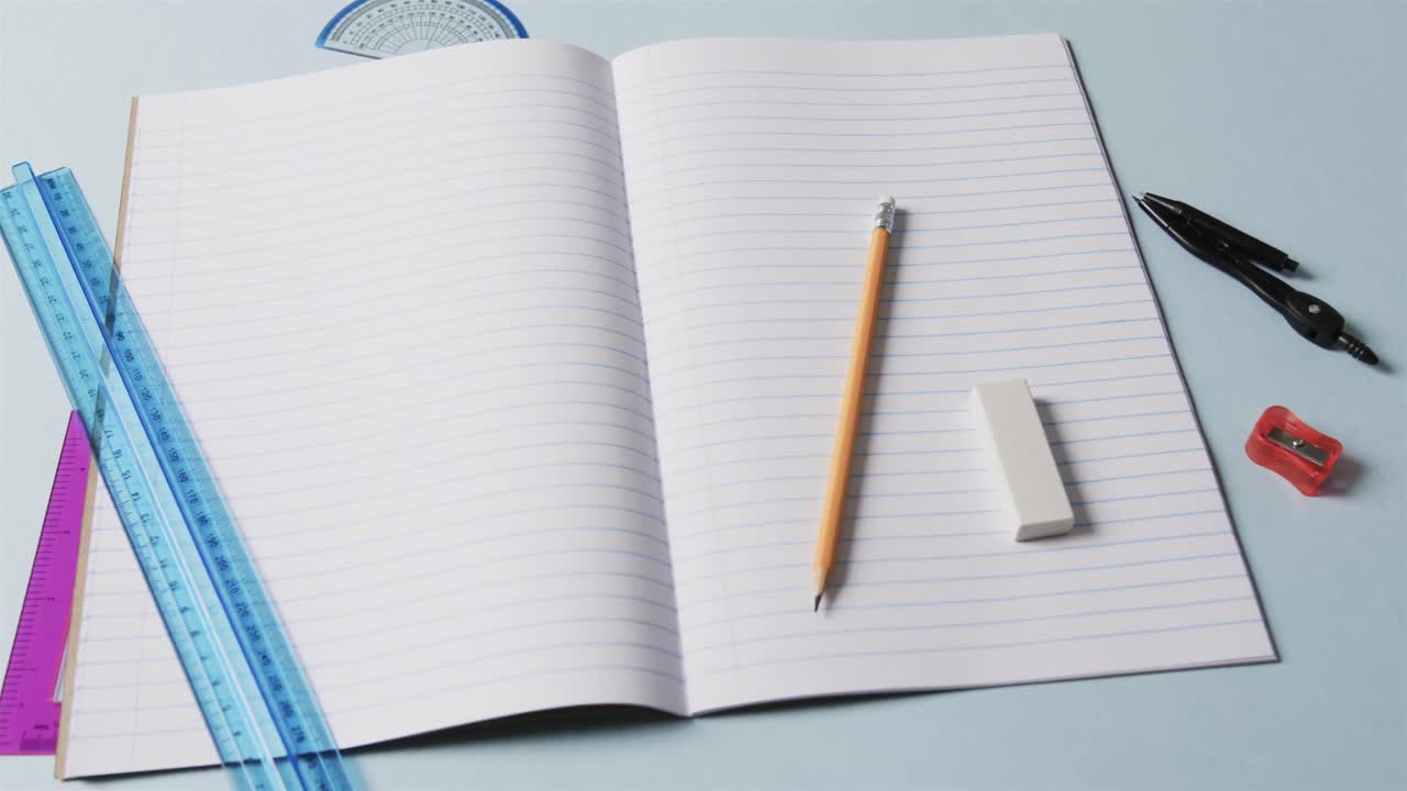 Close up of open notebook with school stationery on blue background, in slow motion