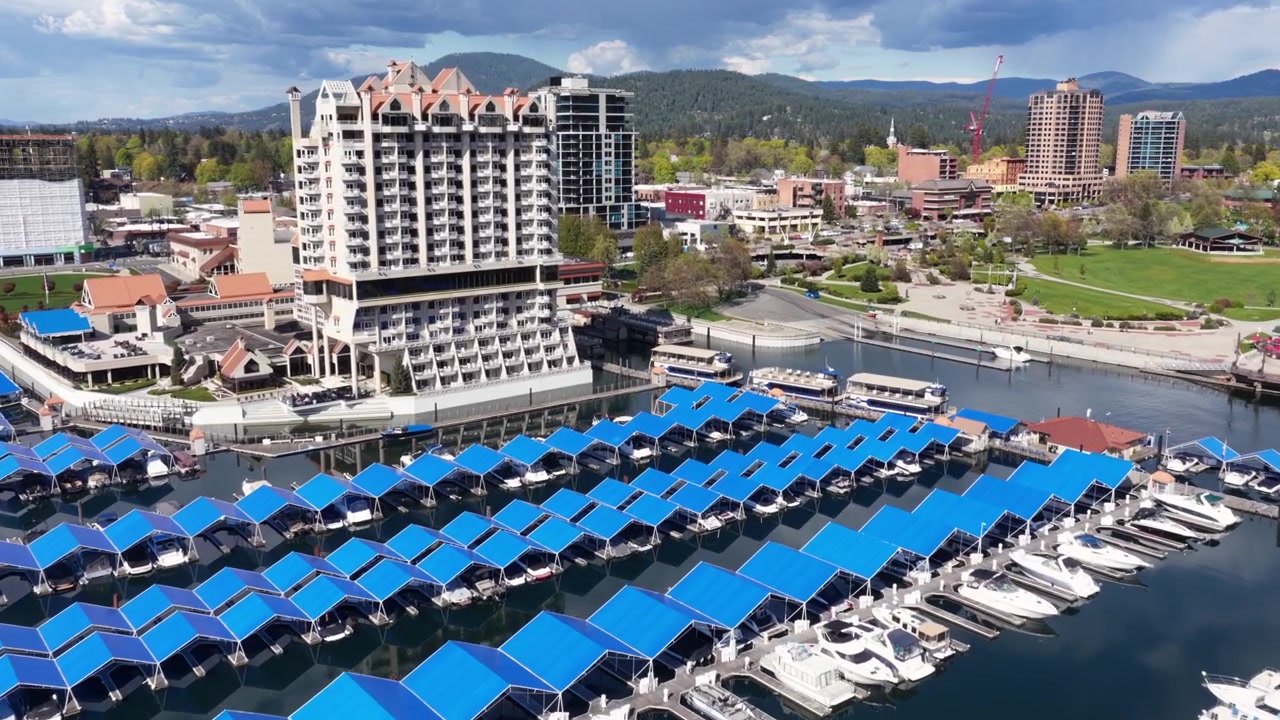 Coeur d'Alene Resort e marina con ormeggi per barche dal tetto blu sul lago Coeur d'Alene, che mostra l'architettura sul lungolago e il paesaggio montano in Idaho, Stati Uniti. Sorvolo aereo.
