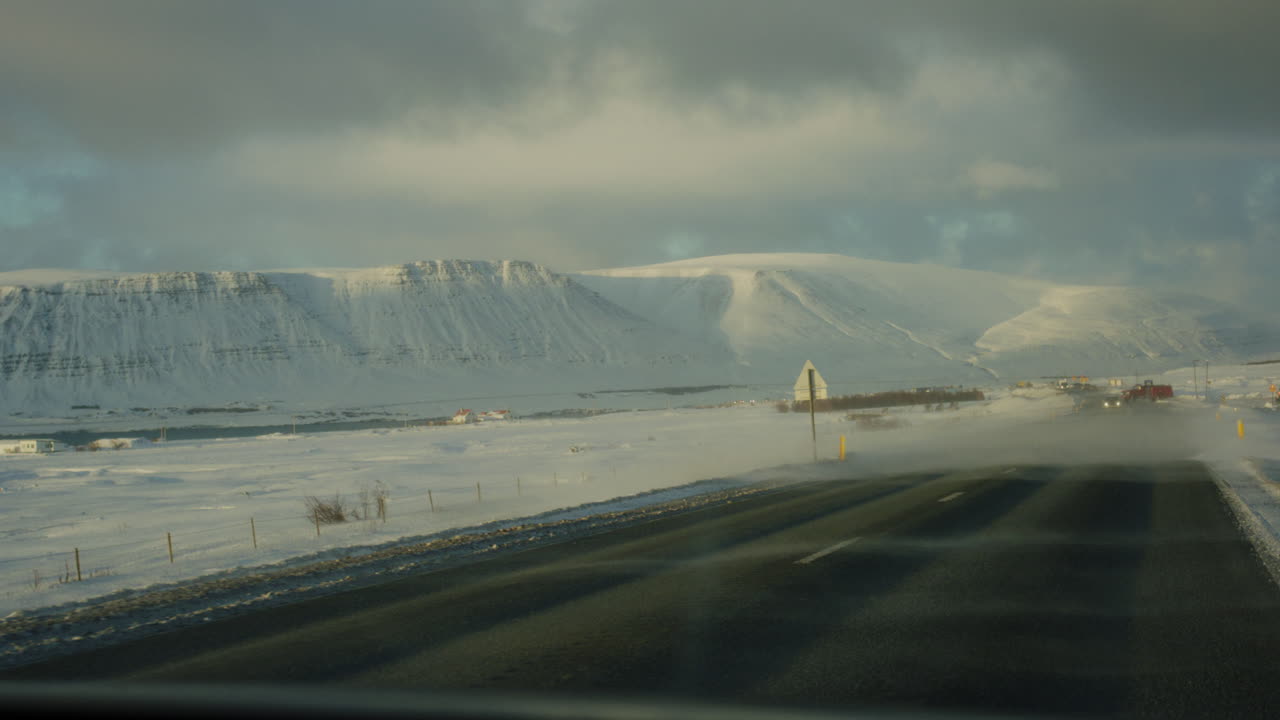 Icelandic road disappearing into snowy horizon under cloudy skies, peaceful winter view, driving POV