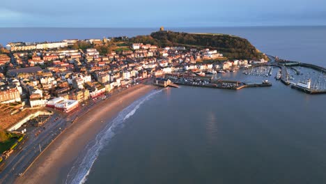 aerial parallax shot of and old town with a small hill beside the harbor with boats in scarborough north yorkshire, england