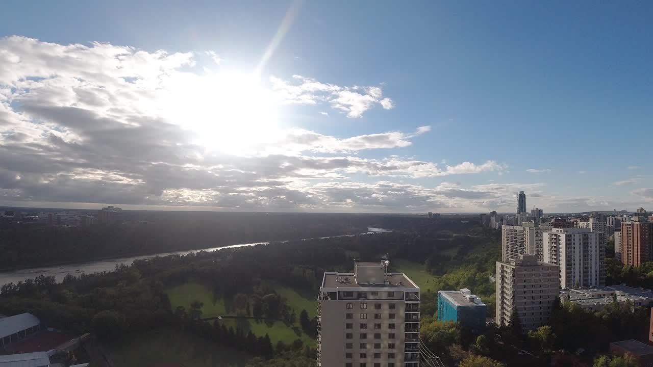 Nuvens aglomeradas se dissipando durante um pôr do sol sobre um parque no vale, separado por um rio largo e imponente entre uma comunidade residencial no centro da cidade e o outro lado sendo um campus universitário com moradias de luxo.