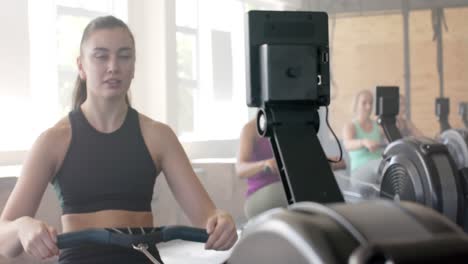 Mujeres-Diversas-Enfocadas-E-Inalteradas-Haciendo-Ejercicio-En-Máquinas-De-Remo-En-El-Gimnasio,-En-Cámara-Lenta