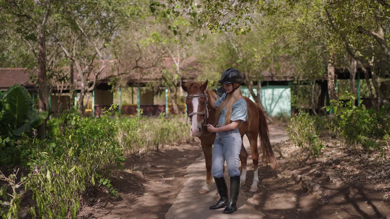 Una donna accarezza dolcemente un cavallo marrone mentre indossa un casco e dei jeans. La scena evidenzia un legame emotivo calmo, fiducia e connessione tra uomo e animale in un ambiente esterno sereno.