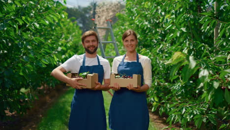 Family-farmers-showing-harvest-cherry-holding-fruit-crate-in-greenhouse-garden.