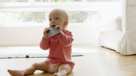 Hermosa-Niña-Sentada-En-El-Suelo-Y-Mordiendo-El-Teléfono-Inteligente