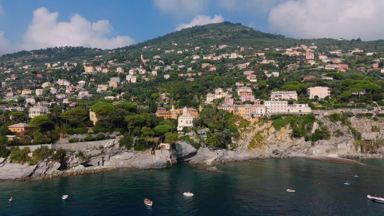 Ripresa con allontanamento del drone che rivela una città costiera, scogliere e mare in Liguria, Italia