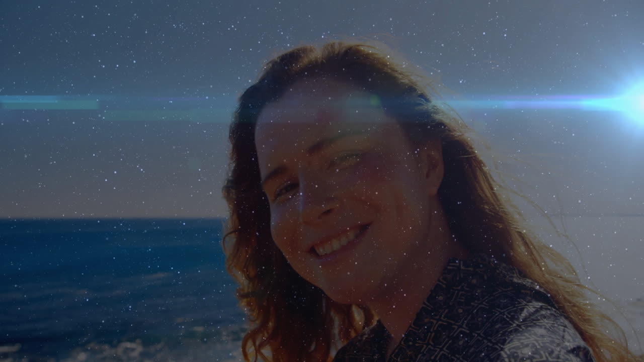 Animation of person smiling by ocean with sparkling light effects in background