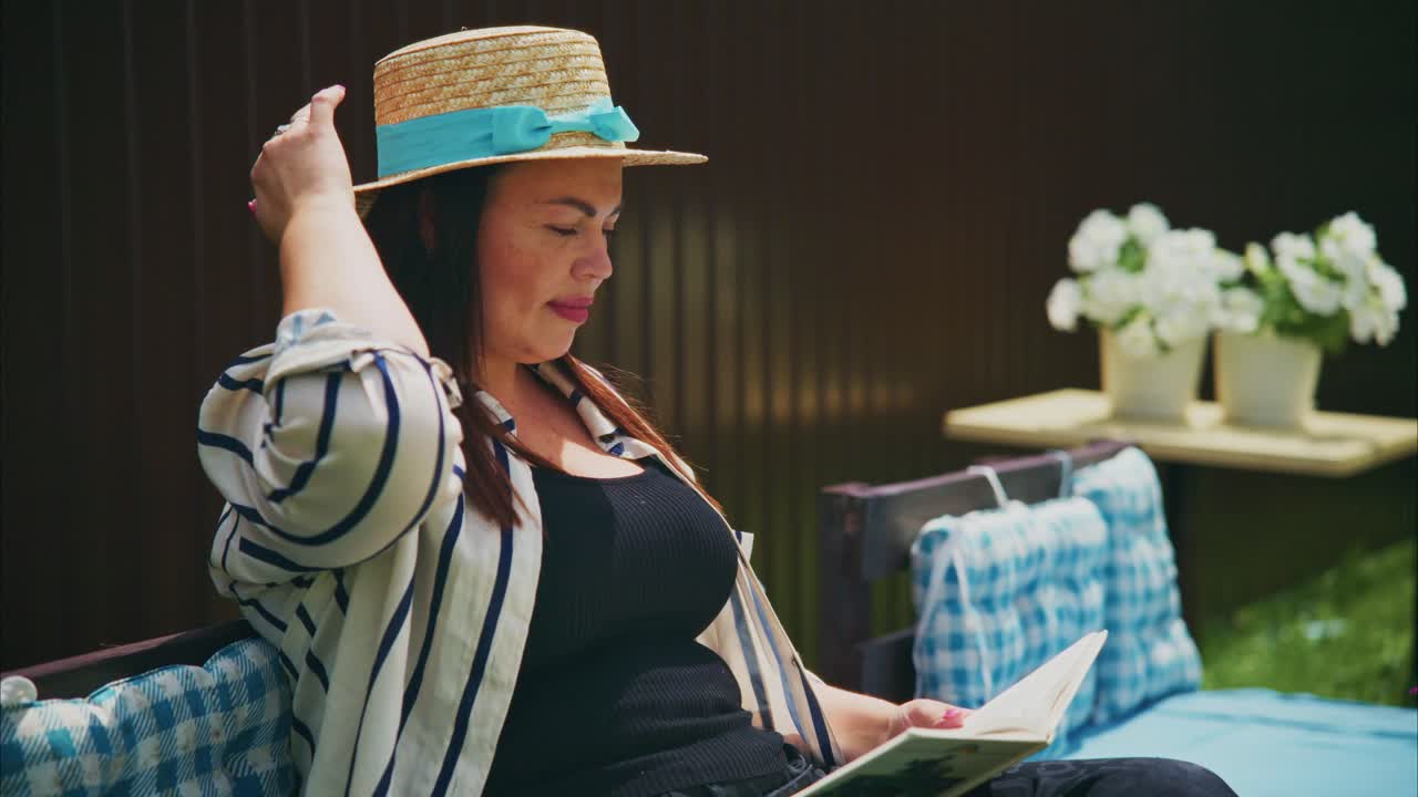 Woman in striped shirt wearing a straw hat reading a book outdoors in a serene garden setting
