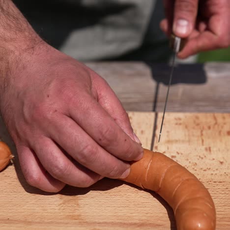 man's hands prepare sausages for barbeque. chef in doing incisions on juicy sausages with a knife on a wooden board before grilling the outdoors. close-up