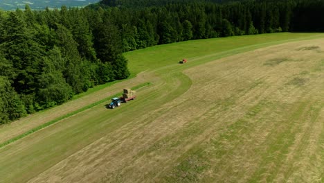 Harvest time on a sunny summer meadow in the Czech countryside — a tractor collecting hay, captured from above by a drone.