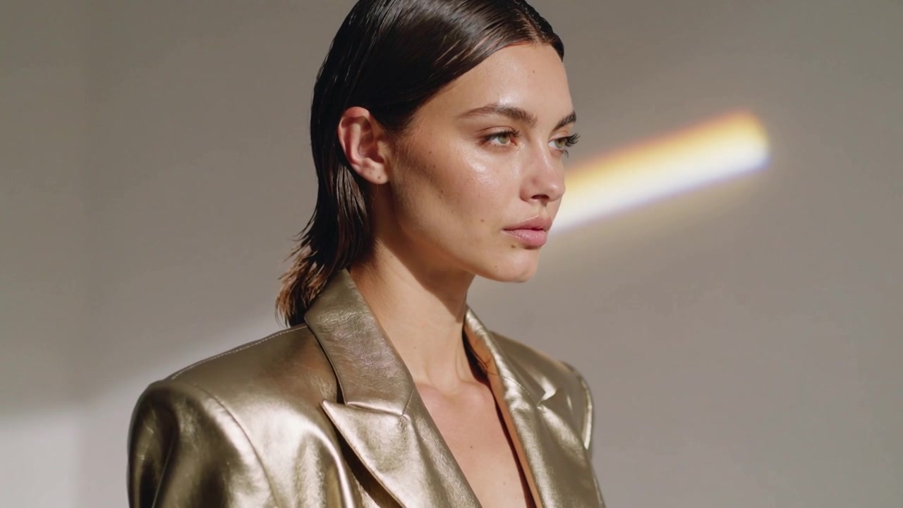 Modella in posa che effettua micro-spostamenti mentre una luce calda la illumina per uno scatto in studio, indossando un blazer dorato.