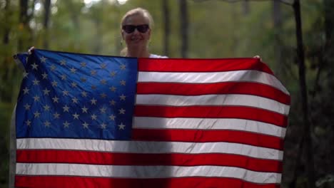 closeup of a pretty mature woman wearing sunglasses and smiling plays with an american flag by waving it up and over her head and then down in front of her