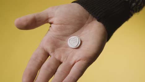 close up of hand holding heart candy with true love message on yellow background 1