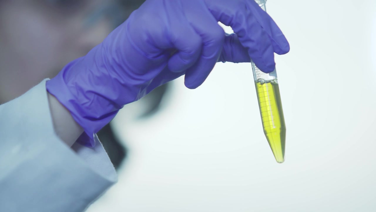 A scientist dissolving yellow coloured chemical in a test tube by shaking.