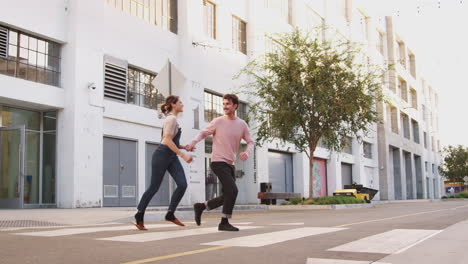 millennial hipster couple running across the road in the city holding hands, full length