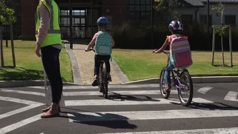 Rückansicht-Von-Zwei-Mädchen-Mit-Schultaschen,-Die-Fahrrad-Fahren-Und-Die-Straße-überqueren