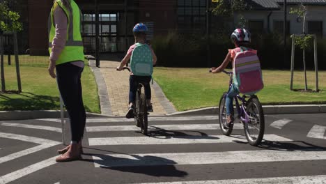 rear view of two girls with school bags riding bicycles and crossing the road