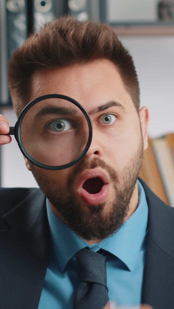 Business man holding magnifying glass near face looking with big zoomed eye searching analysing