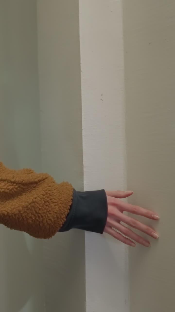 A close-up shot of a girl wearing a brown coat and carrying a black backpack as she gently touches a wall with her hand. sense of contemplation and the tactile connection with the surroundings