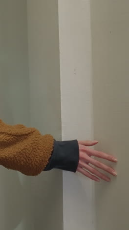 una toma de primer plano de una chica con un abrigo marrón y llevando una mochila negra mientras toca suavemente una pared con su mano. sentido de contemplación y la conexión táctil con el entorno