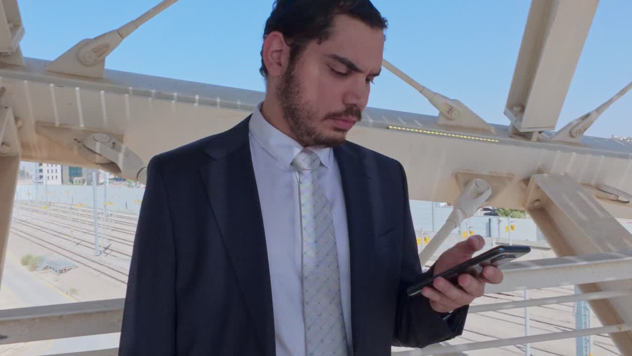 Uomo d'affari in abito che controlla il suo smartphone su un cavalcavia urbano