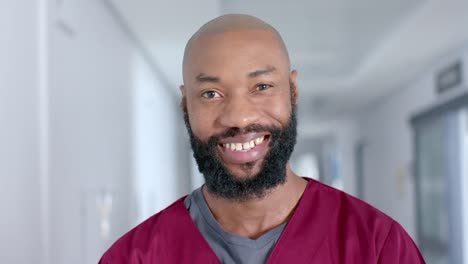 portrait of happy african american male doctor wearing scrubs in corridor, slow motion