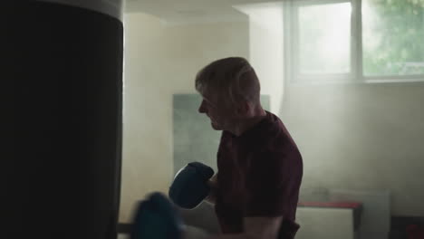 sportsman exercises beating punching bag in sports center. excited man punches equipment training in foggy gym slow motion. martial arts champion