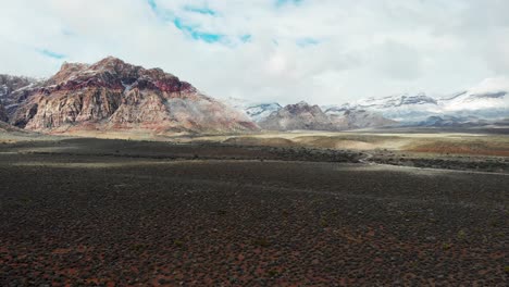 Aerial-drone-shot-along-the-desert-with-mountains-and-clouds-in-the-background