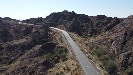 aerial drone view of a car racing down a lonely highway in the desert mountains of balochistan