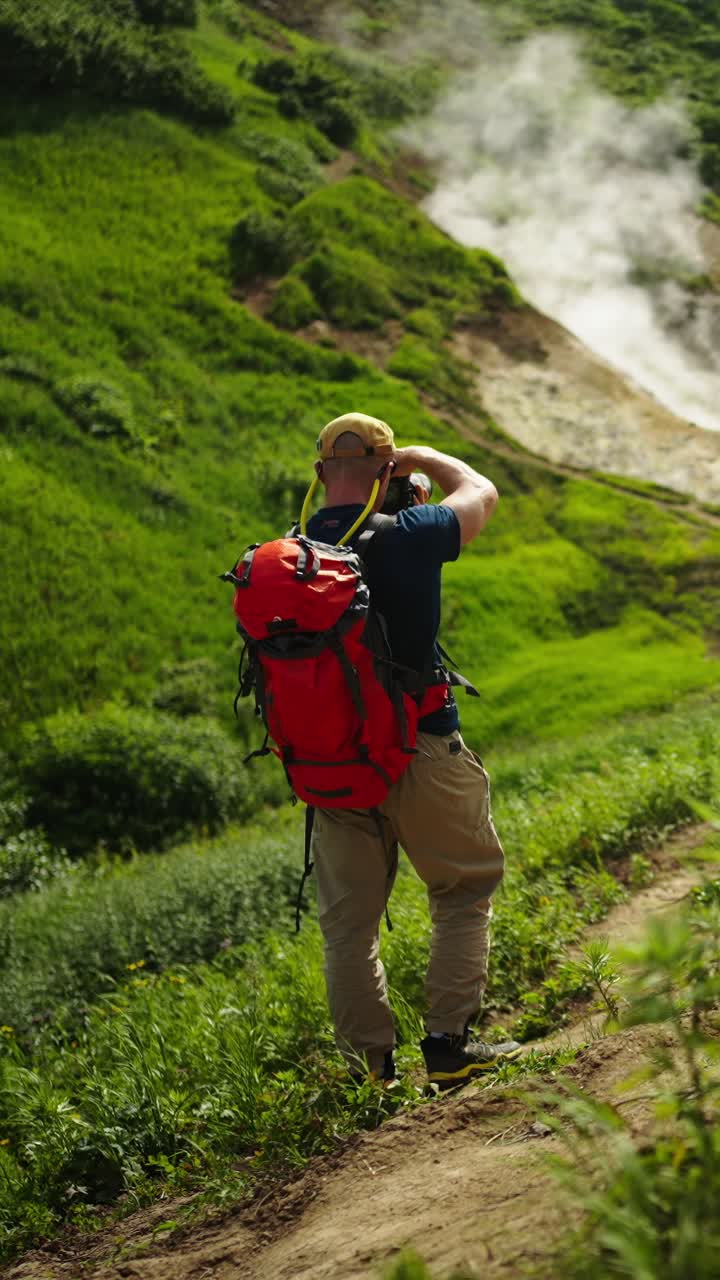 Uomo con zaino che scatta foto in un paesaggio vulcanico verde