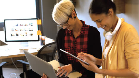 dos mujeres ejecutivas de negocios interactuando a través de tabletas digitales y portátiles