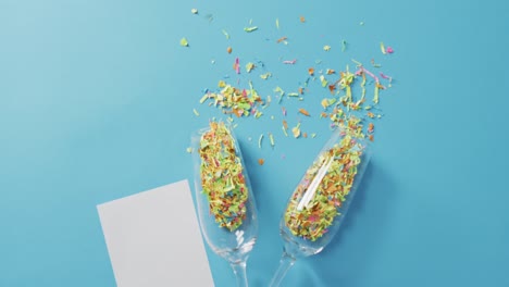 Champagne-glasses-with-confetti-and-white-card-on-blue-background-at-new-year's-eve
