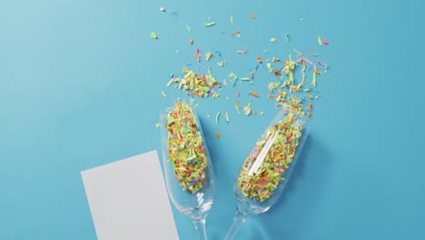Champagne glasses with confetti and white card on blue background at new year&#039;s eve